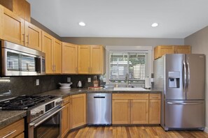A modern kitchen with wooden cabinets, stainless steel appliances, a dishwasher, and a window with blinds. - Star Lake Waterfront Estate (Auburn)