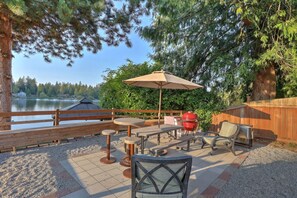 An outdoor patio with a table, chairs, a grill, and a view of a lake.
