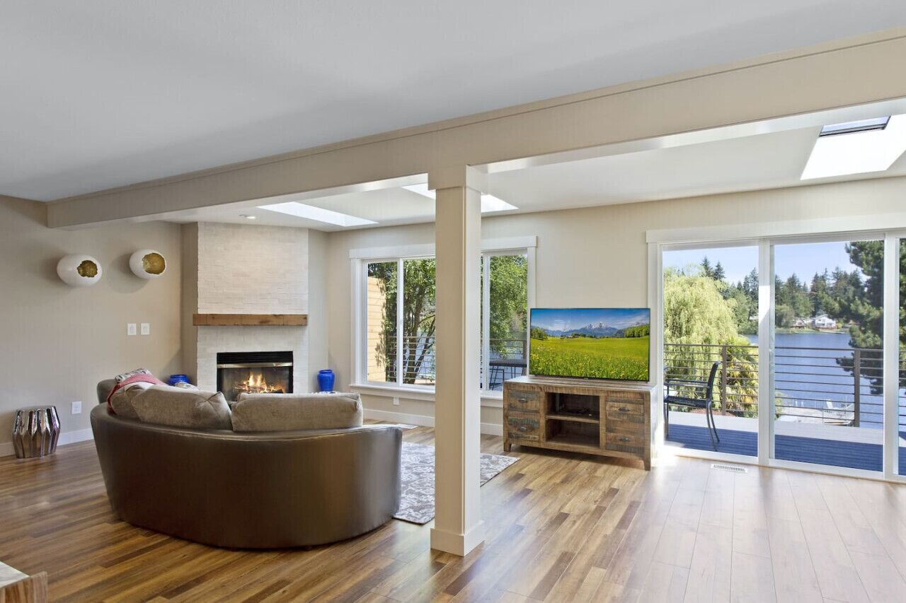 A spacious living room with a fireplace, a large TV, and a view of a lake through sliding glass doors.