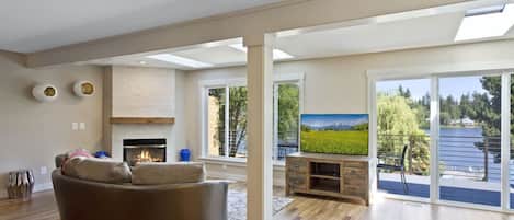 A spacious living room with a fireplace, a large TV, and a view of a lake through sliding glass doors.