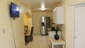 A kitchen with a refrigerator, a dining area with chairs, and a small table with a vase.