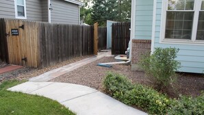 A backyard with a wooden fence, a concrete pathway, and a small garden area.