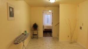 A hallway with a patterned floor, a small table with an ironing board, a potted plant, and a staircase leading to a bedroom.
