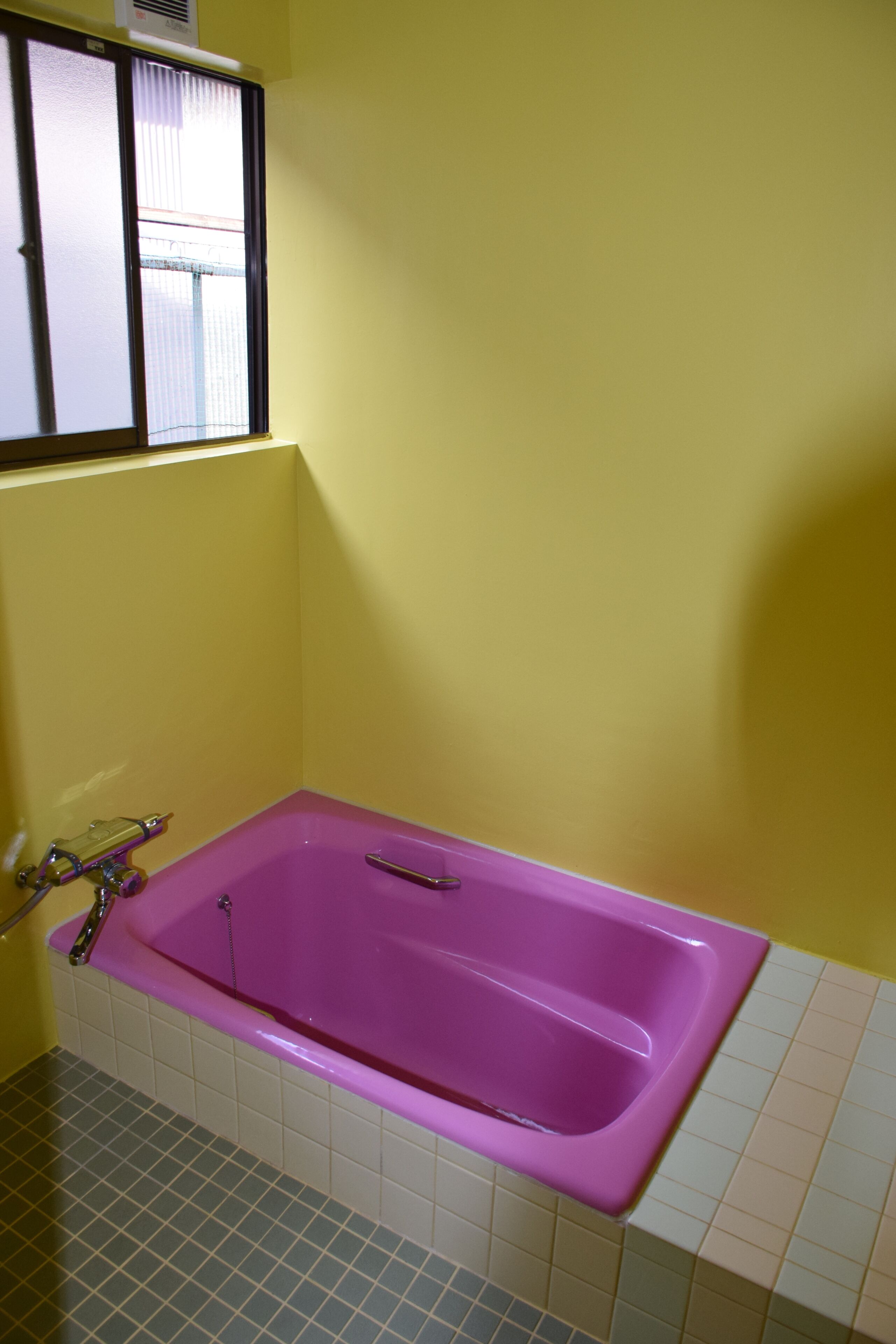 Un baño con una bañera morada, paredes amarillas y una ventana con persianas.
