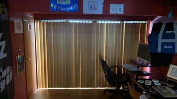 A room with a desk, computer, and a window with blinds.