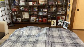A bedroom with a plaid bedspread, a bookshelf filled with various items, and a small desk with a lamp.
