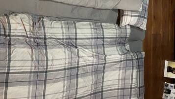 Una cama con una manta y almohadas a cuadros, un cabecero de madera y una mesita con una revista.