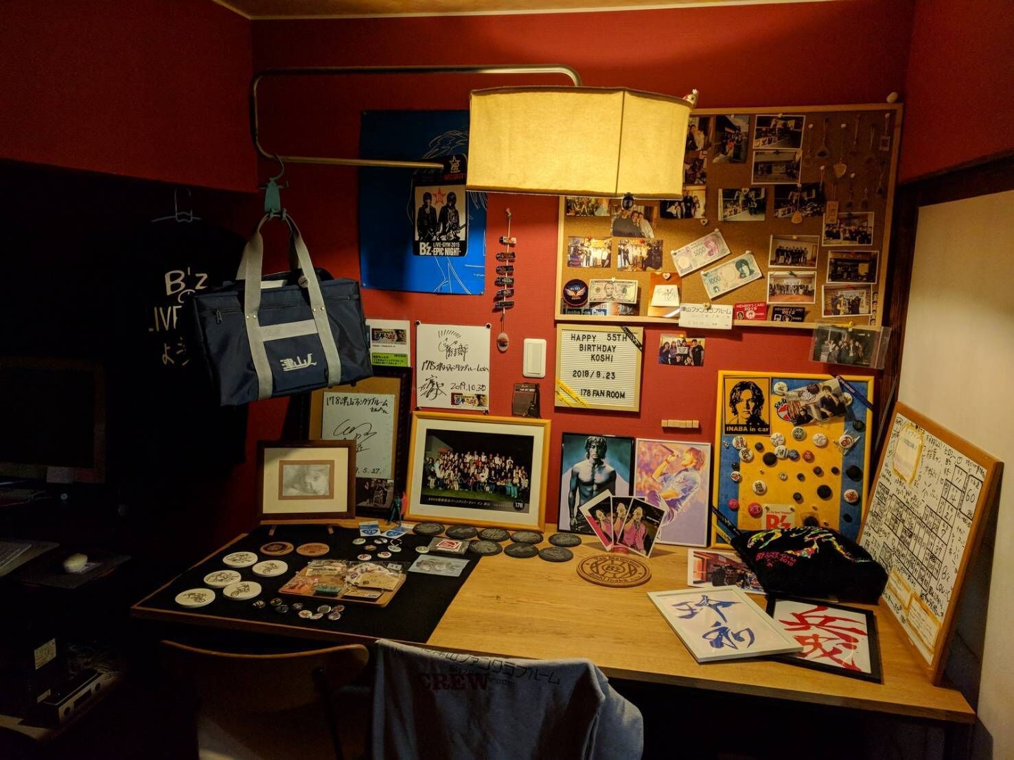 A room with a desk cluttered with memorabilia, a hanging bag, and various photos and posters on the wall.
