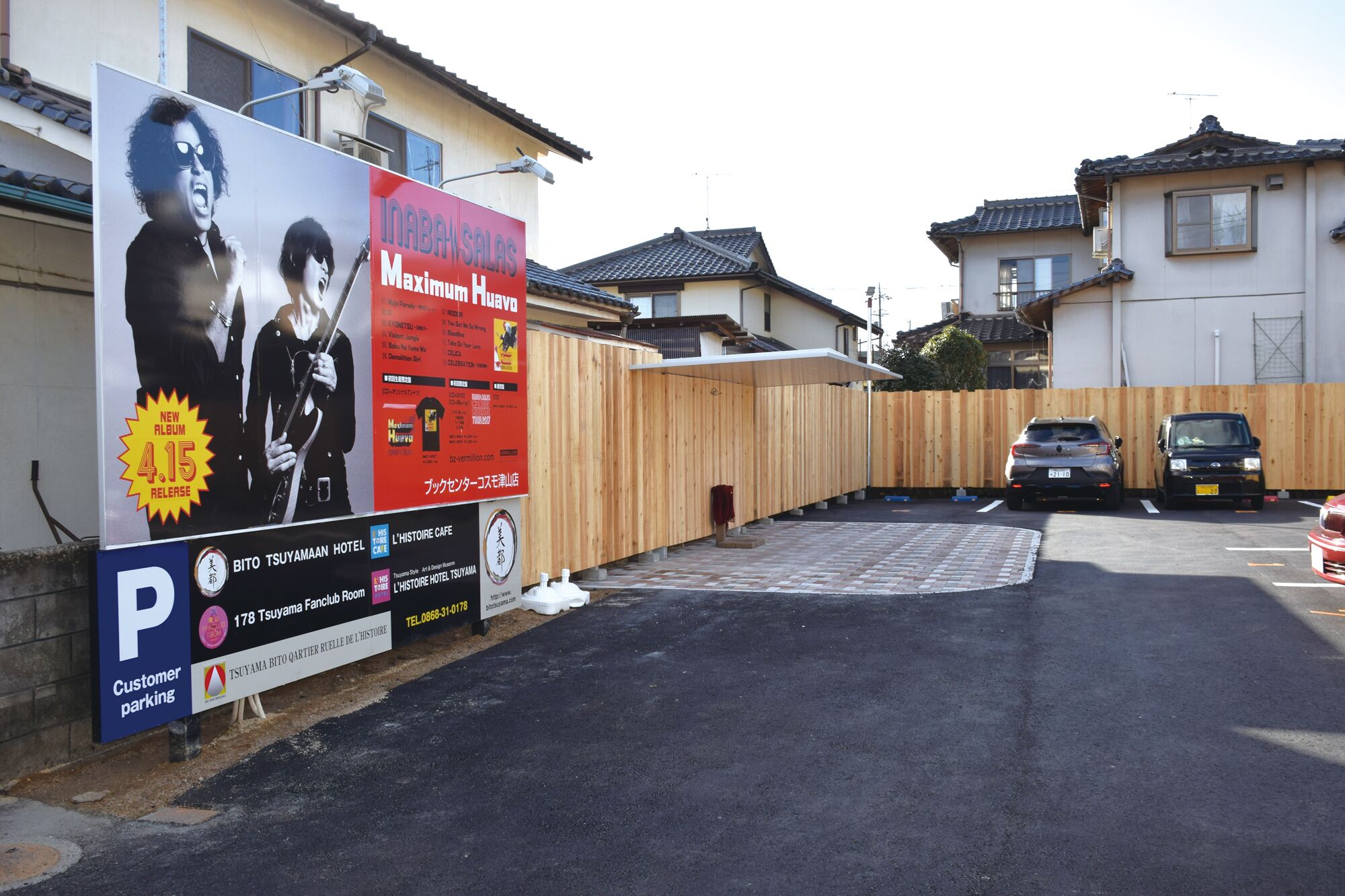 A hotel entrance with a wooden fence, a parking area, and a signboard advertising a new album release.