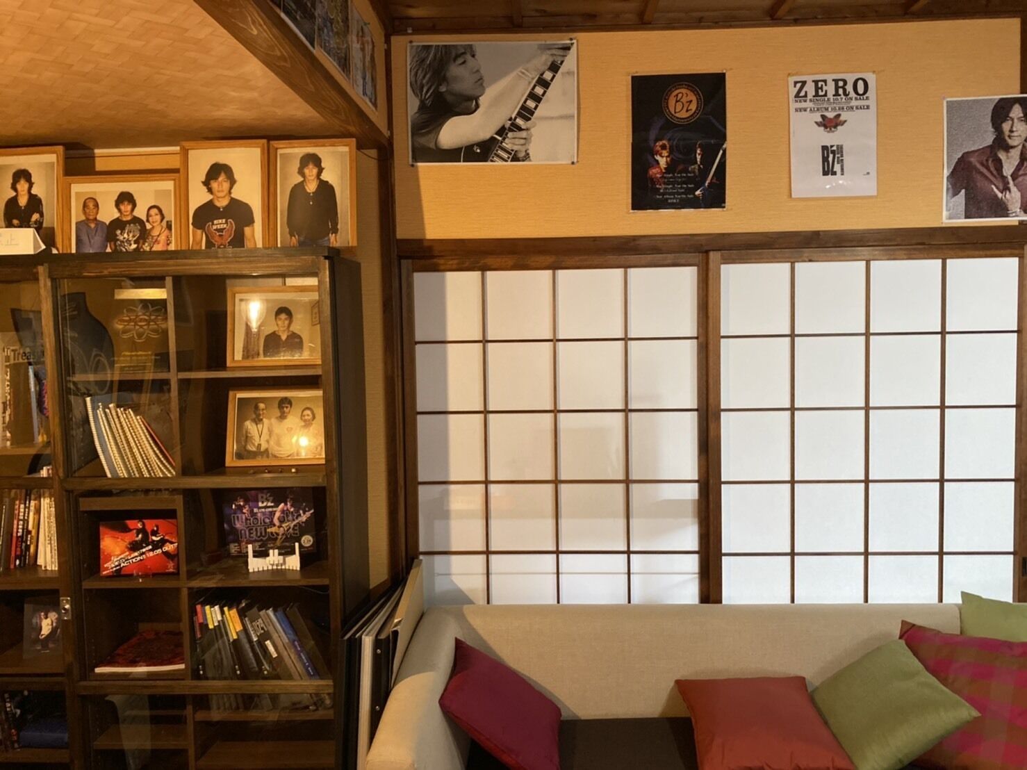 A room with a bookshelf filled with books and CDs, a sofa with colorful cushions, and a shoji screen door.