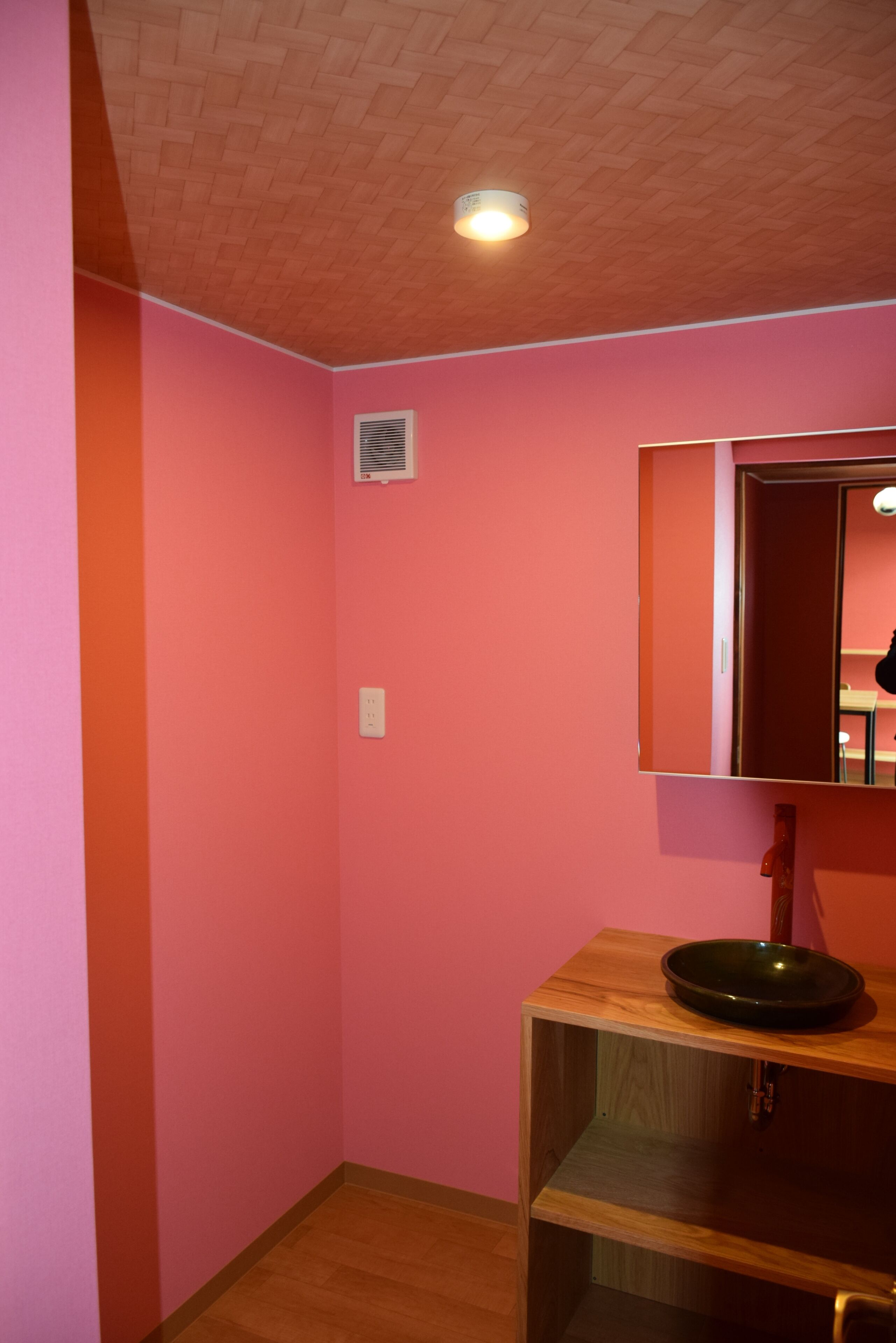 A room with pink walls, a wooden floor, a mirror, and a small shelf with a bowl.
