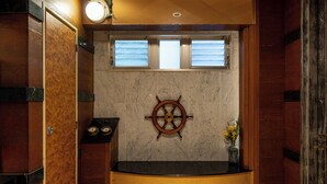 A bathroom with a wooden vanity, a ship's wheel decoration, and a vase with flowers.