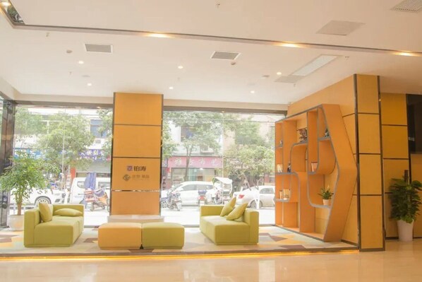 A modern hotel lobby with a reception desk, seating area, and large windows offering a view of the street. - Chonpines Hotel (Guangyuan)