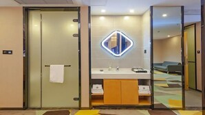 A modern bathroom with a glass partition, a mirror with a neon light, and a towel hanging on the door. - Chonpines Hotel (Guangyuan)