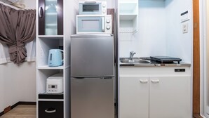 A compact kitchen with a refrigerator, microwave, kettle, and a small countertop with a sink. - Togano house Umeda central (Osaka)