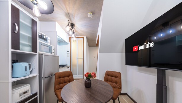 A modern kitchen with a dining table, chairs, a vase with flowers, and a flat-screen TV mounted on the wall. - Togano house Umeda central (Osaka)