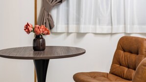 A room with a round table, a vase with flowers, a brown leather chair, and a window with curtains. - Togano house Umeda central (Osaka)