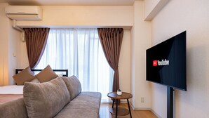Ein modernes Hotelzimmer mit Sofa, Bett, Fernseher und einem kleinen Tisch.