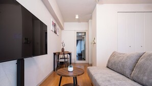 Ein gemütlicher, kleiner Wohnbereich mit einer Couch, einem runden Tisch, einem Fernseher und einer Tür zu einem anderen Zimmer.
