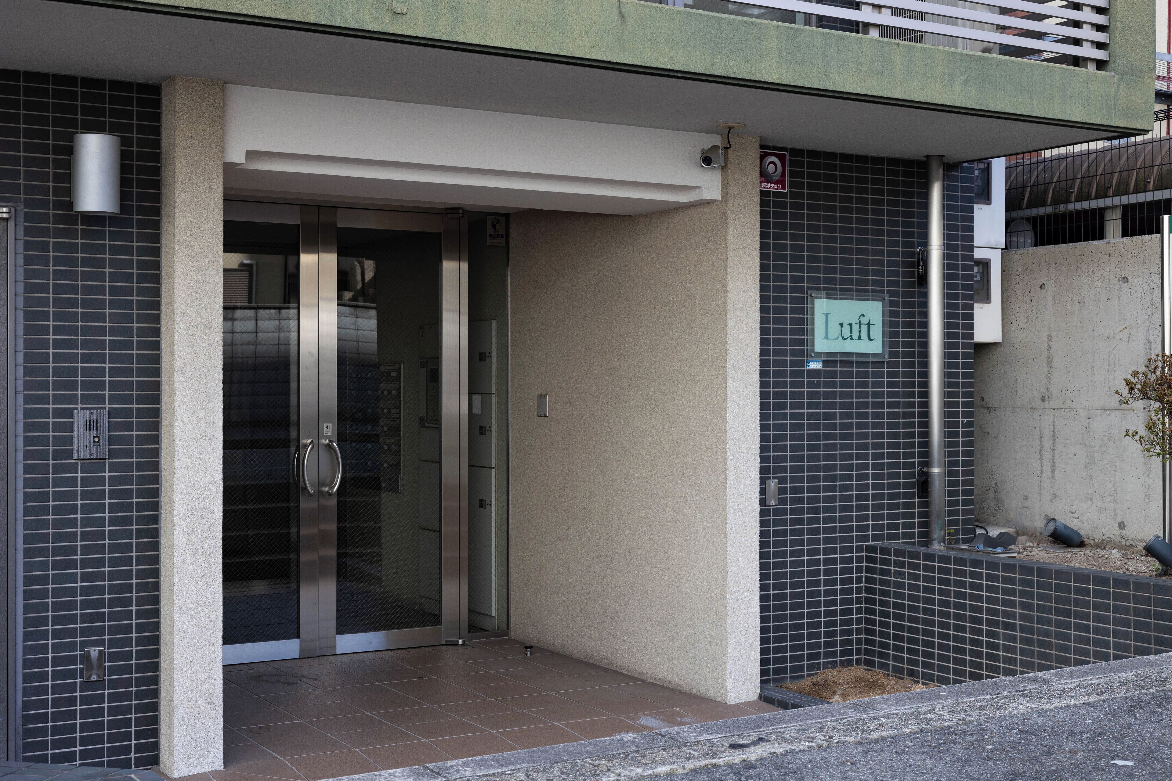Fachada de un edificio con puerta de cristal, un cartel que dice "Luft" y revestimiento de baldosas.