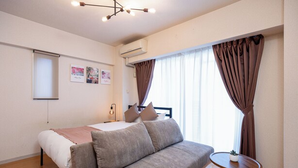 Ein modernes Schlafzimmer mit einem Bett, einer Couch, einem kleinen Tisch und einem Fenster mit Vorhängen.