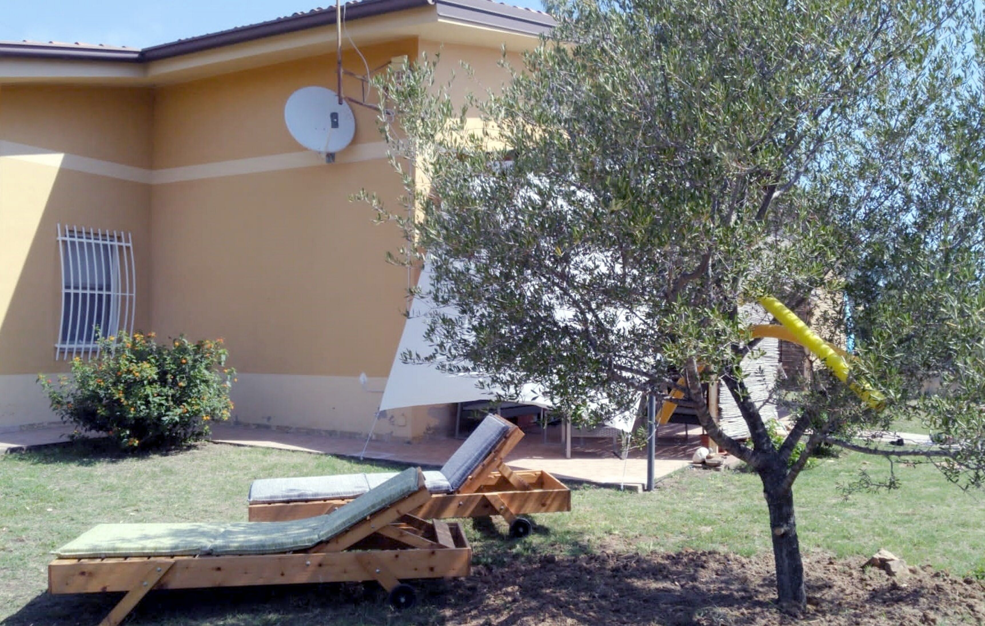 Ein Haus mit Satellitenschüssel, einem Baum und einer Holzterrasse mit Liegestuhl.