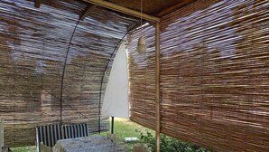 An outdoor patio with a table and chairs, covered by a woven shade structure. - Base Camp Ogliastra - Flat Green  (Santa Maria Navarrese)