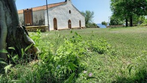 A white building with a tiled roof and arched windows, surrounded by greenery and a clear sky. - Base Camp Ogliastra - Flat Green  (Santa Maria Navarrese)
