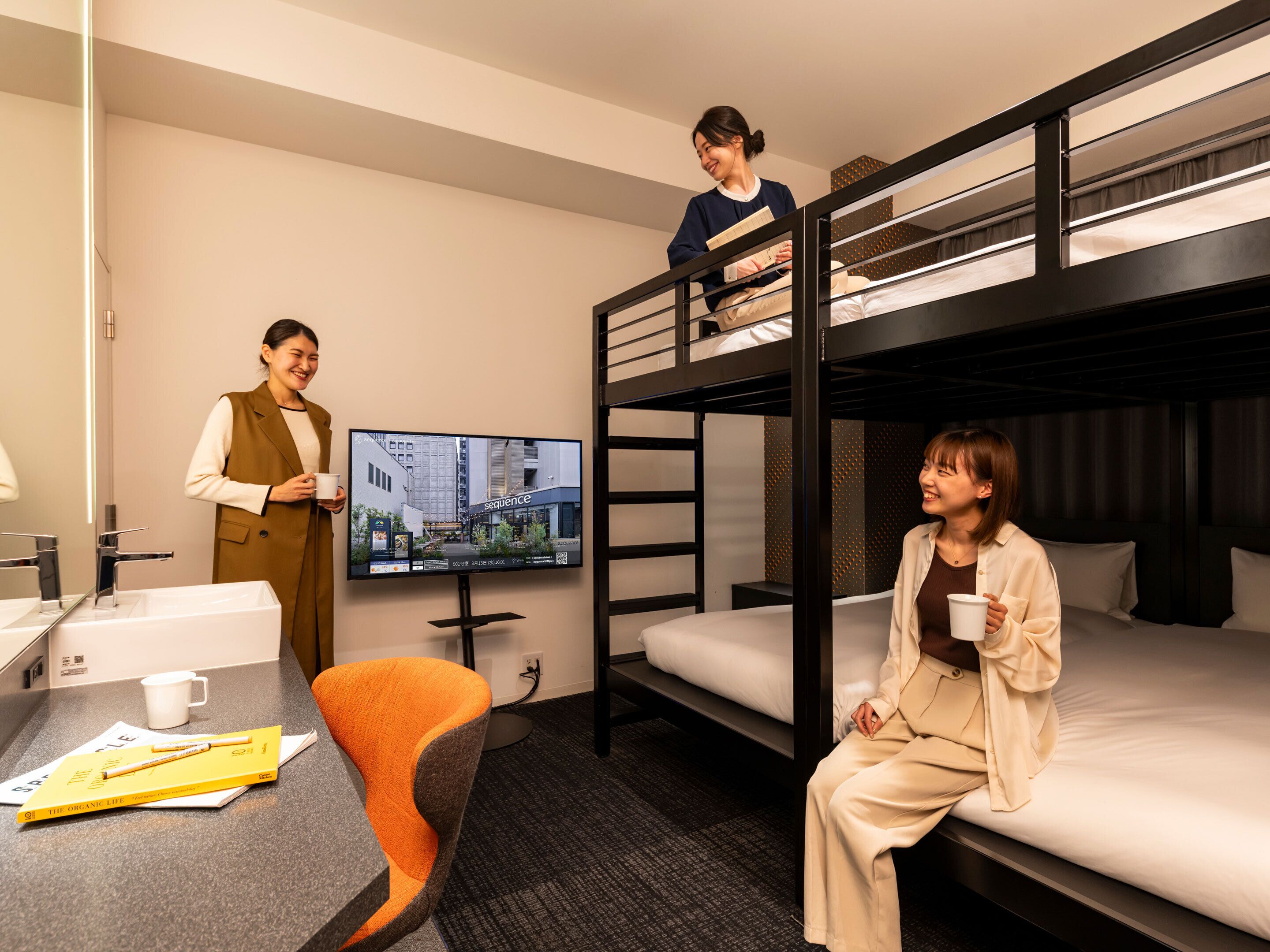 A hotel room with bunk beds, a desk with a chair, a television, and a coffee cup.