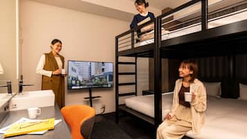 A hotel room with bunk beds, a desk with a chair, a television, and a coffee cup.