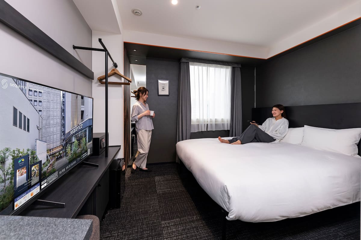 Quarto de hotel com uma cama grande, televisão, escrivaninha e janela com cortinas.