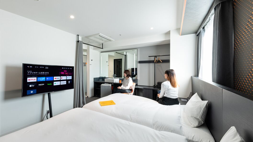 Una habitación de hotel moderna con una cama grande, un televisor de pantalla plana mostrando servicios de streaming, un escritorio con una silla y un espejo.