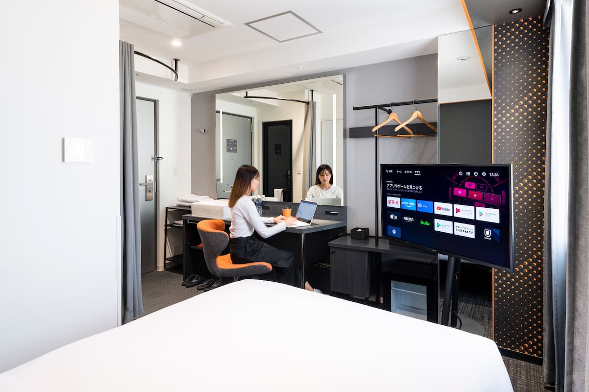 Quarto de hotel moderno com uma cama grande, uma escrivaninha com um laptop, uma televisão de tela plana e um espelho.