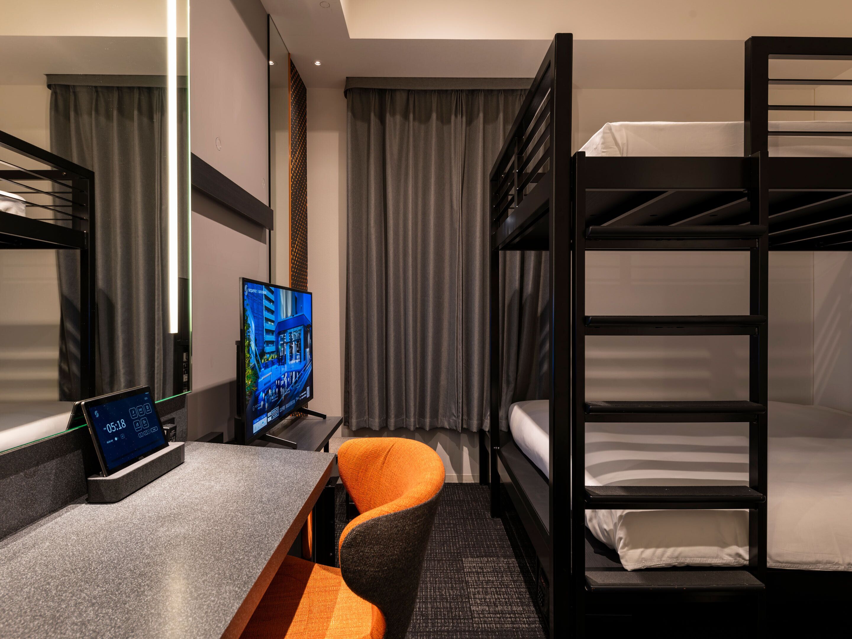 A hotel room with a bunk bed, a desk with a computer monitor, and a chair.