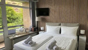 A hotel room with a bed, two bedside tables, a TV, and a view of greenery outside.
