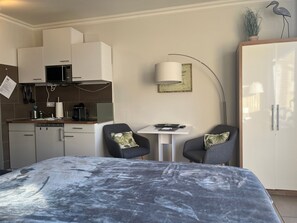 Un dormitorio moderno con cama, escritorio y silla. Cuenta con una kitchenette con microondas y estufa.