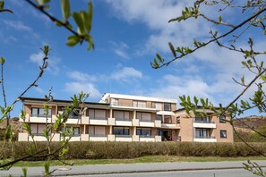 Ein modernes, mehrgeschossiges Gebäude mit Balkonen und großen Fenstern, umgeben von viel Grün und blauem Himmel.