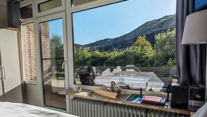 A hotel room with a large window, a bed, a desk with a computer, and a view of a mountainous landscape. - Lister Dünennest, Deutschland (List)