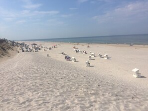 Ein weiter Sandstrand mit vielen Liegestühlen und Sonnenschirmen.