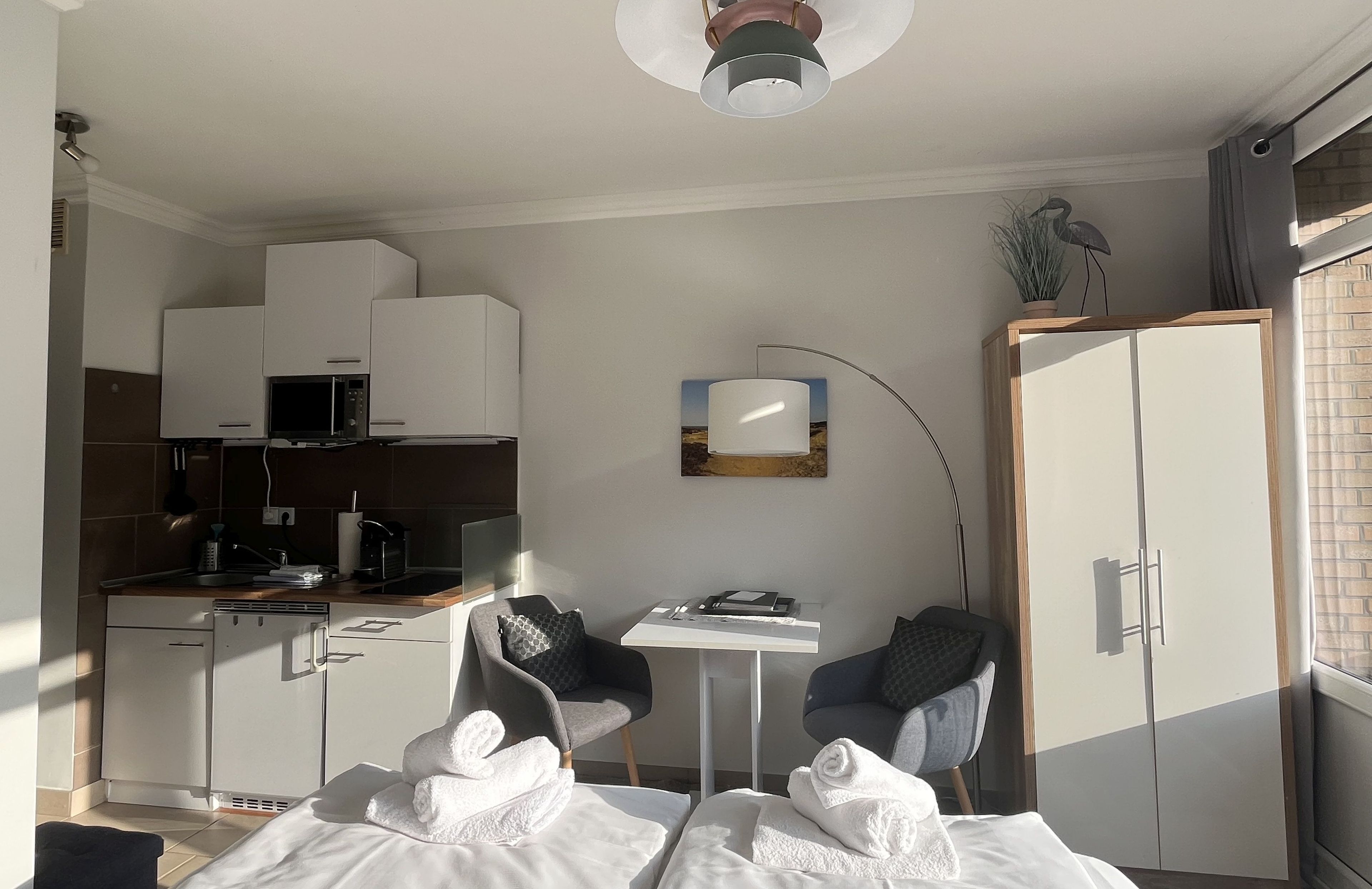 Ein kompaktes Hotelzimmer mit Küchenzeile, Essbereich, einem Bett und Handtüchern sowie Blick ins Freie.