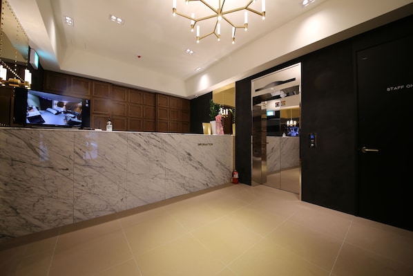 A modern reception area with a marble counter, a television displaying a kitchen scene, and an elevator. - Ninespot Hotel (Daejeon)