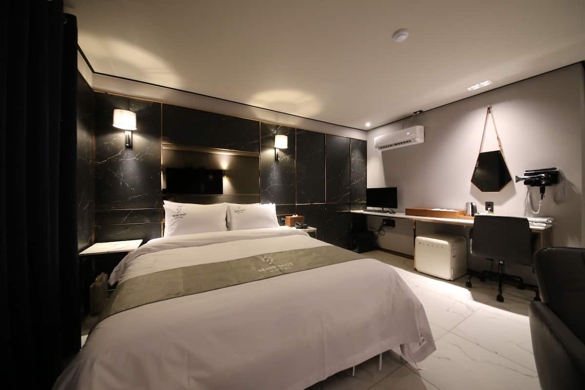Ein Hotelzimmer mit einem großen Bett, Nachttischen, einem Schreibtisch, einem Sessel und einer Wandlampe.