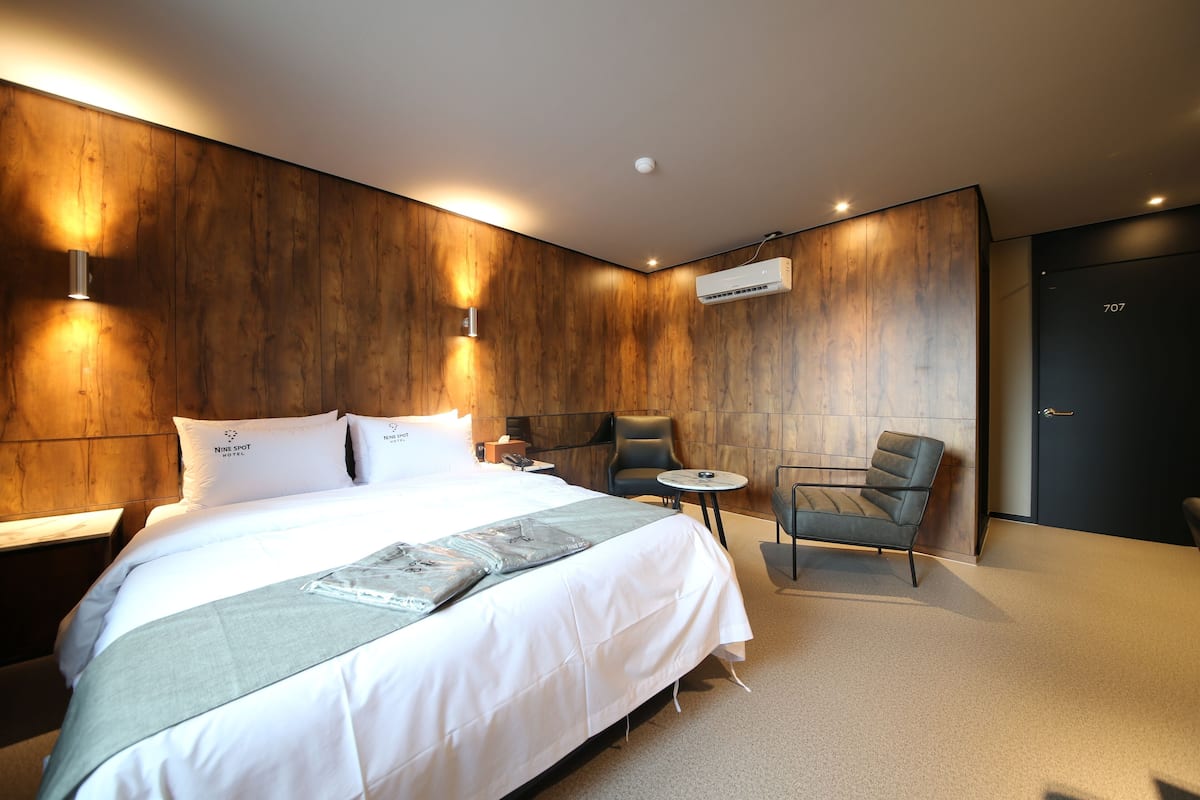 Ein modernes Hotelzimmer mit einem großen Bett, einem kleinen Tisch, zwei Stühlen, einer Wandklimaanlage und einer Tür mit einer Nummer.