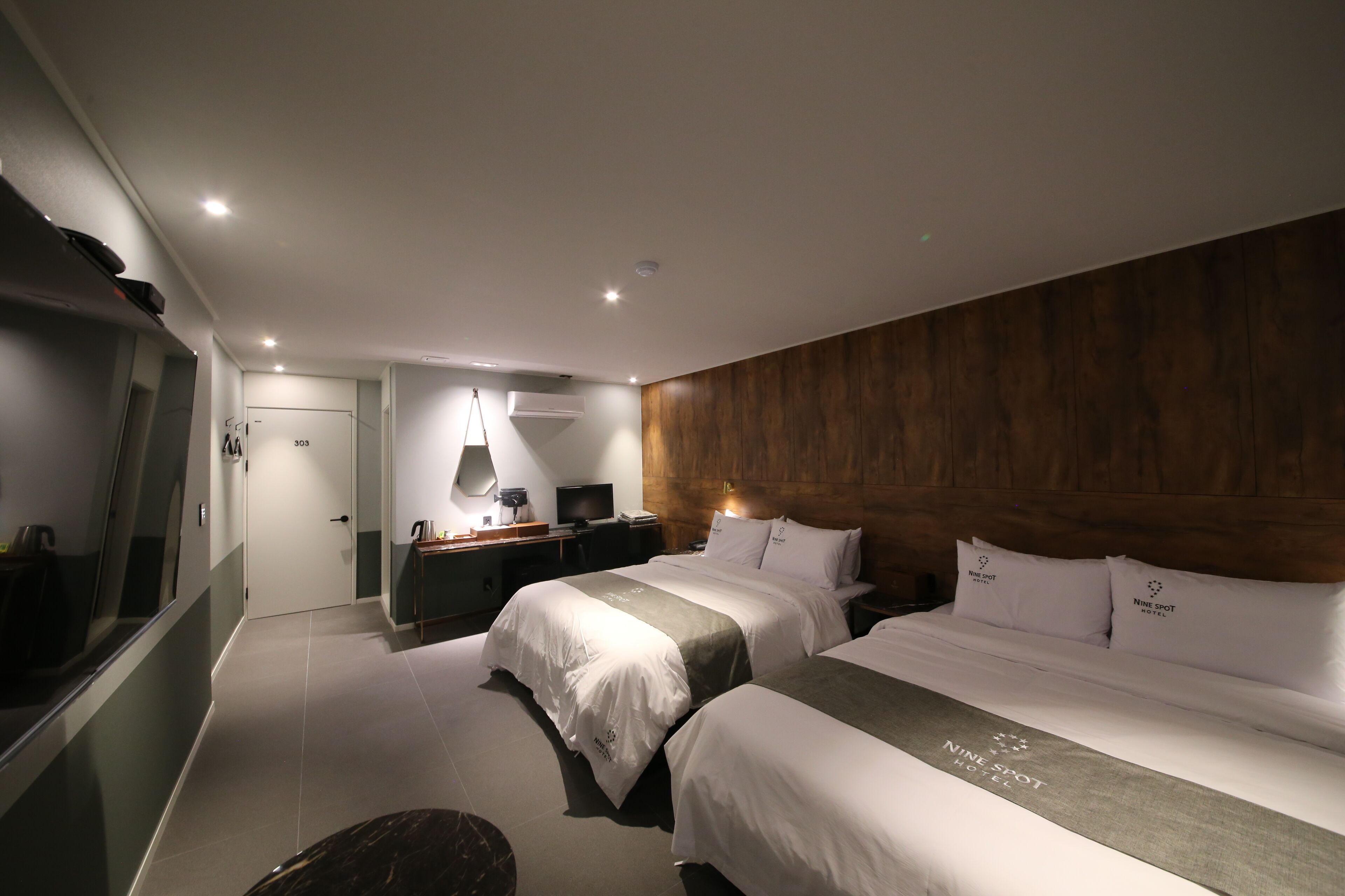 A hotel room with two beds, a desk with a computer, a TV, and a wooden headboard.