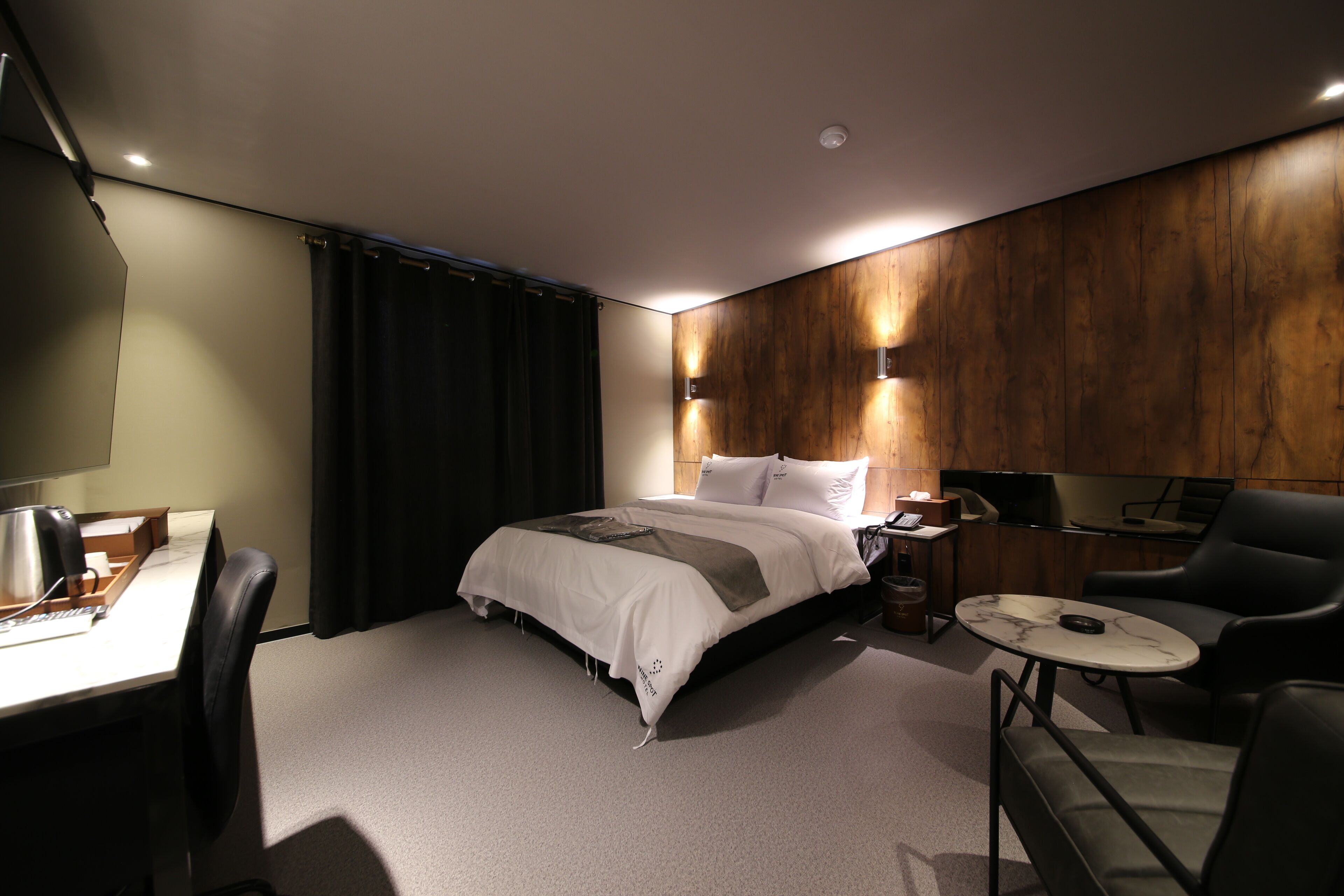 A modern hotel room with a bed, a desk, a chair, and a small table.