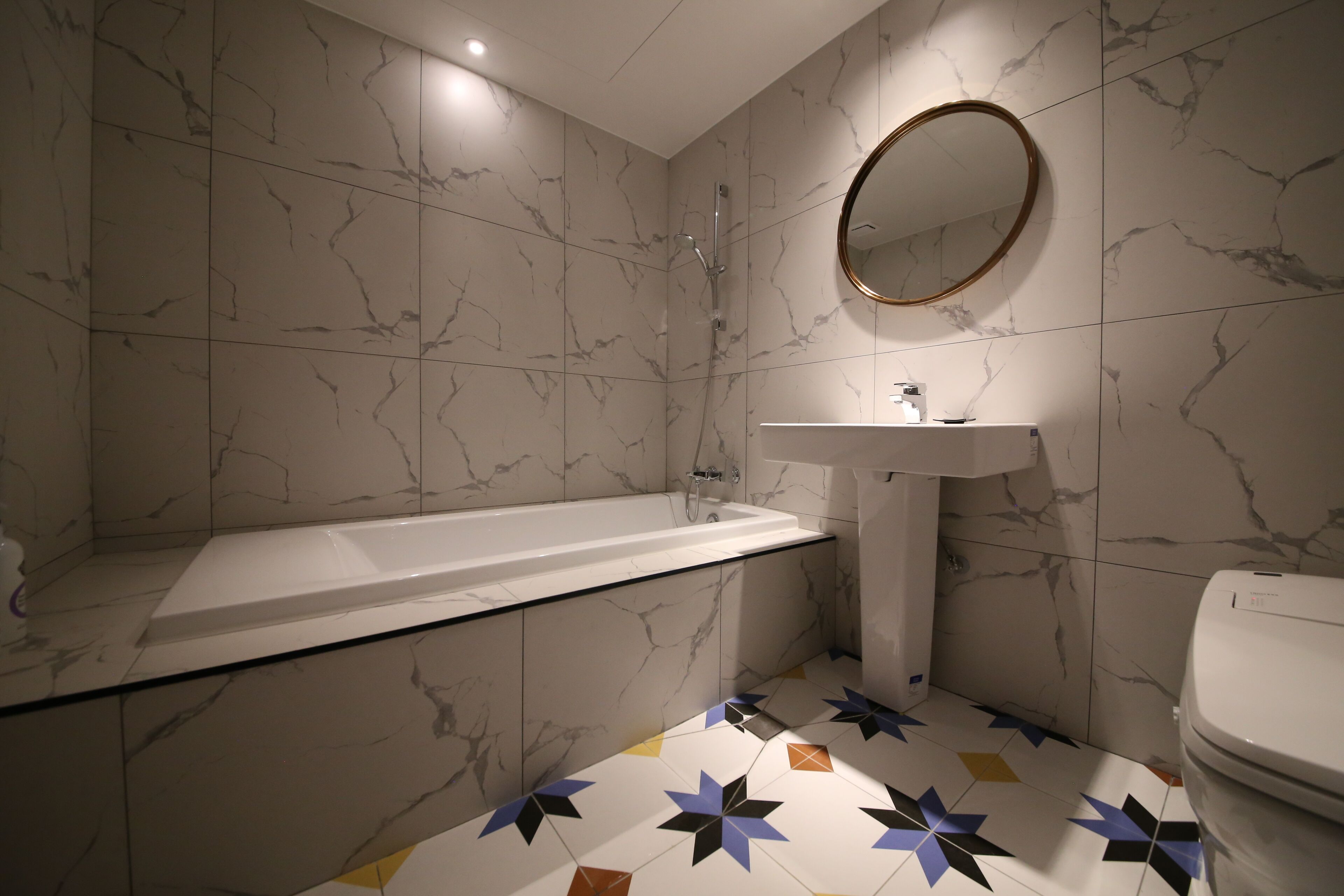 Ein Badezimmer mit einer Wand aus Marmorfliesen, einer weißen Badewanne, einem Waschbecken und einer Toilette.