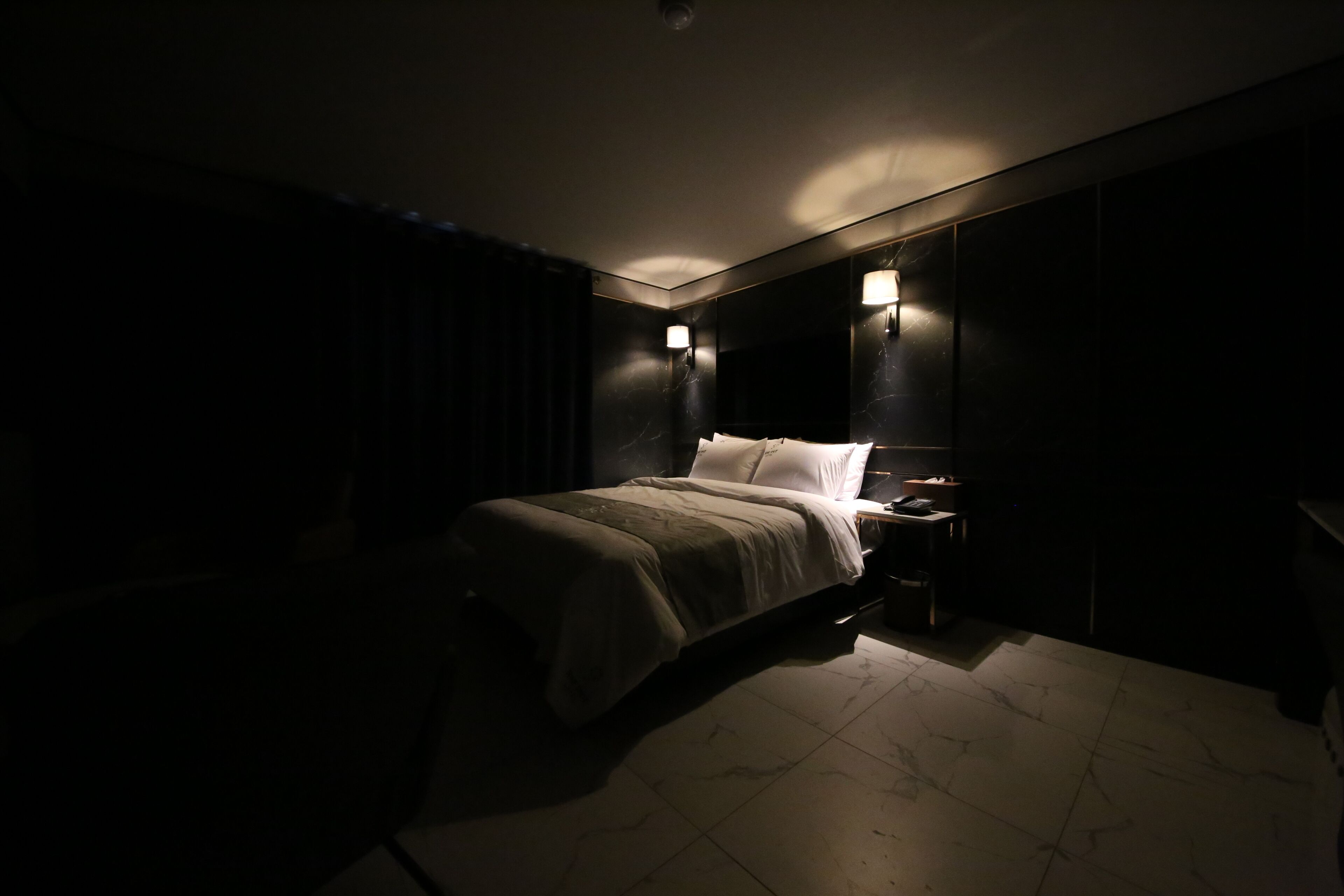 Un habitación de hotel con poca luz, una cama, mesitas de noche y lámparas de pared.
