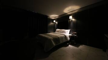 Un habitación de hotel con poca luz, una cama, mesitas de noche y lámparas de pared.