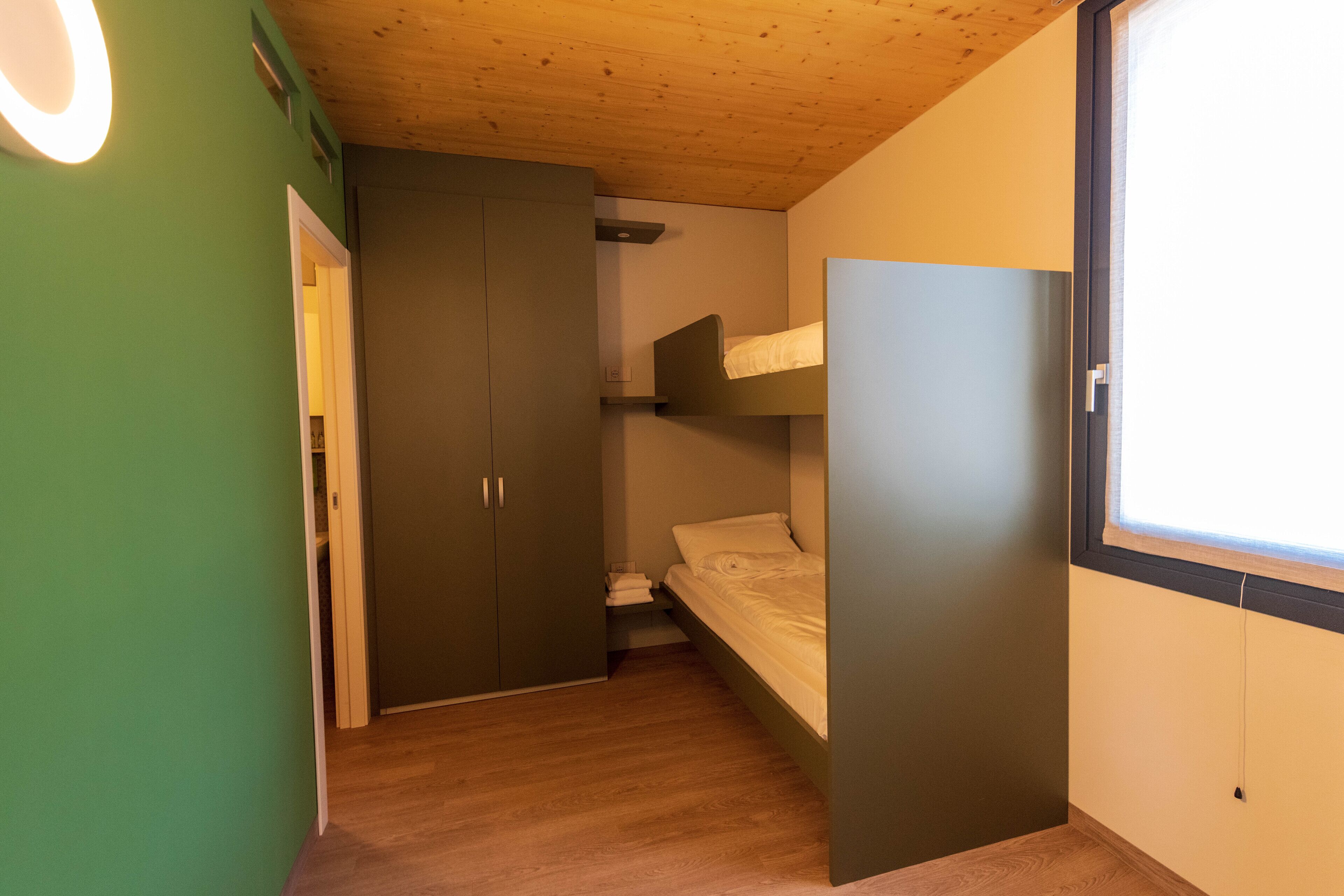 Habitación pequeña con una litera, un armario y una puerta que da a otra habitación.