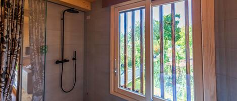 A bathroom with a shower, a bathtub, and a window with a view of greenery.